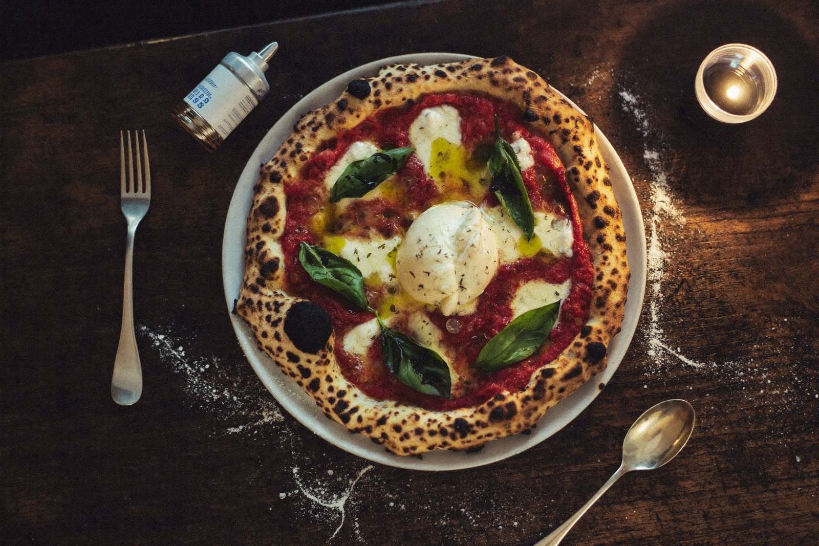 Ofenfrische Pizza mit Burrata und Basilikum auf dunklem Holztisch