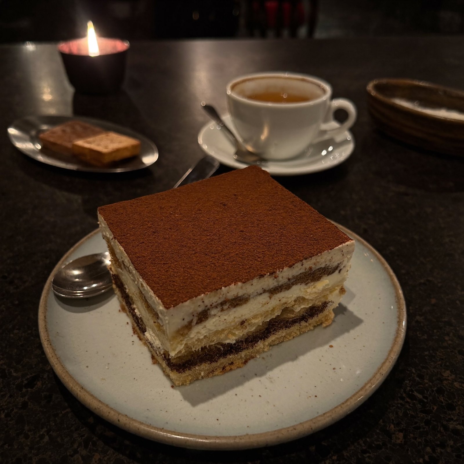 Hausgemachtes Tiramisù mit Kakao, dahinter eine Tasse Espresso